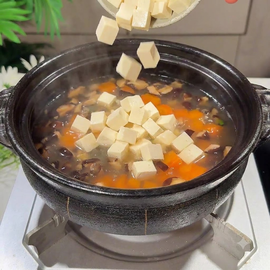 Diced silken tofu pieces falling into the simmering soup pot.