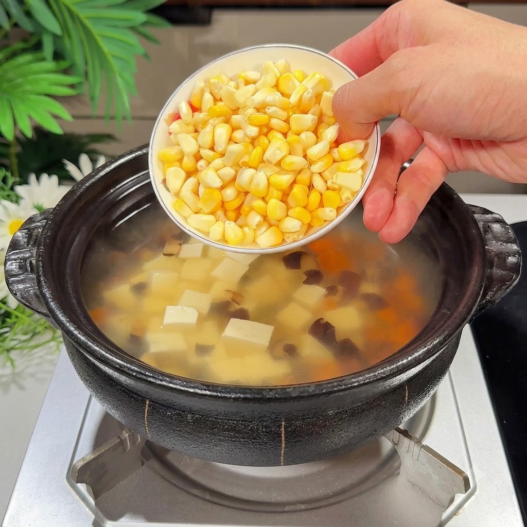 A small bowl of fresh corn kernels being poured into the soup pot.