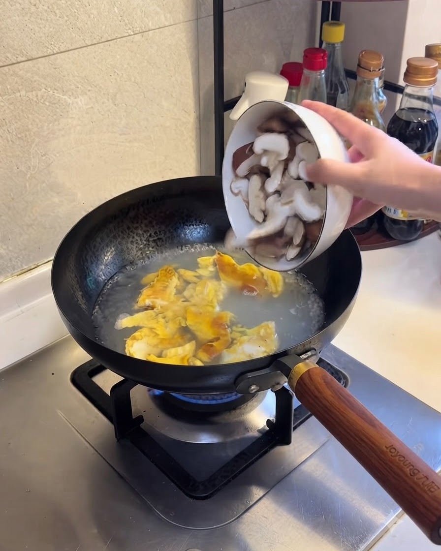 Sliced shiitake mushrooms being added to the boiling water and egg mixture.