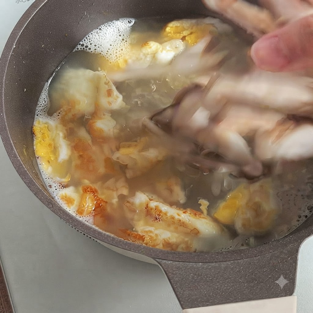 A hand dropping sliced fresh shiitake mushrooms into a boiling broth with fried egg pieces.