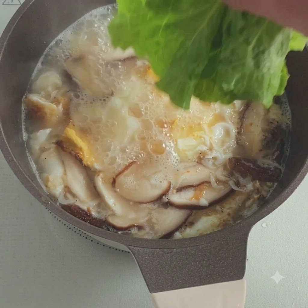 Fresh lettuce leaves being dropped into a pot of bubbling soup with mushrooms and eggs.
