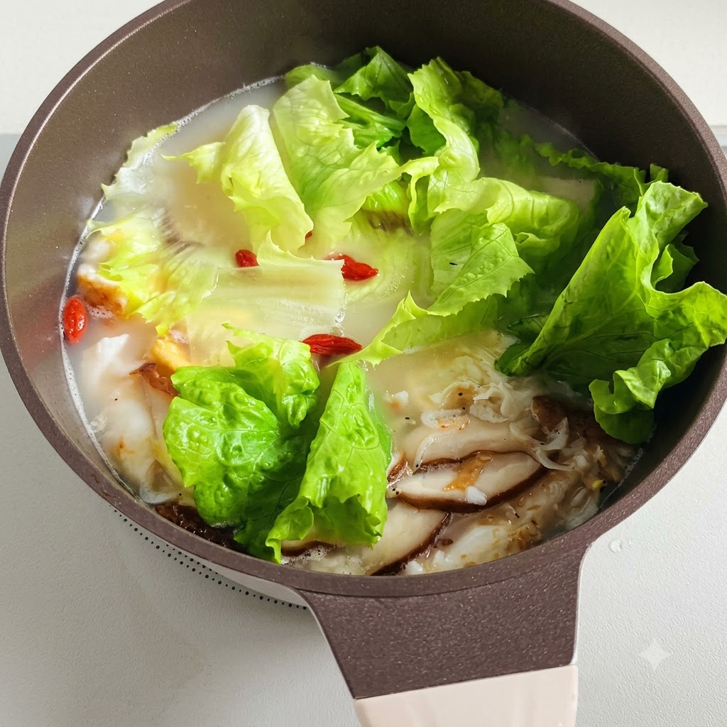 A pot of simmering soup with lettuce leaves and red goji berries floating inside.