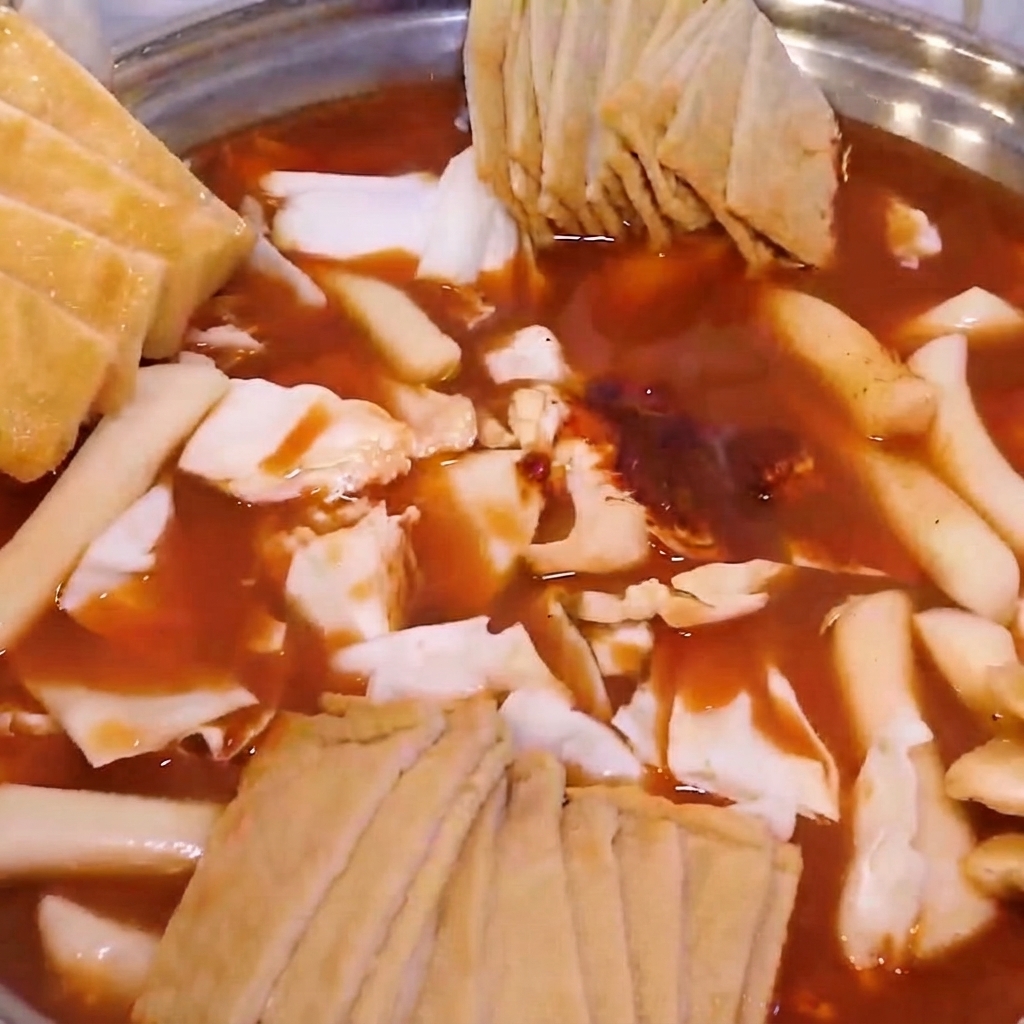 An assembled hot pot filled with cabbage, rice cakes, fish cakes, and topped with fried bean curd and green onions.
