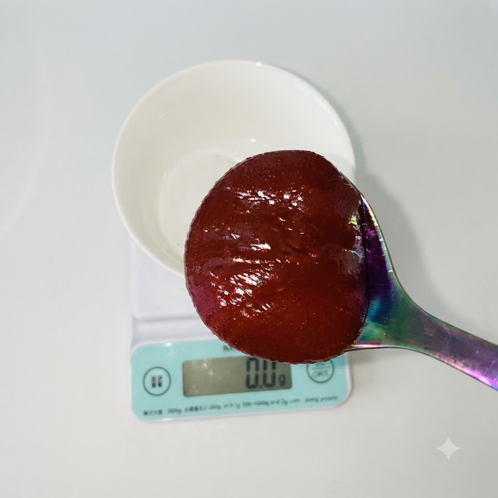 A spoonful of red Korean chili paste being held over a white bowl resting on a digital kitchen scale.