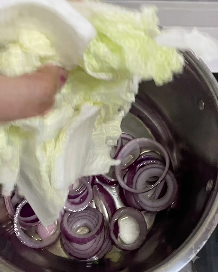 Adding chopped Napa cabbage into the pot over the red onion base.