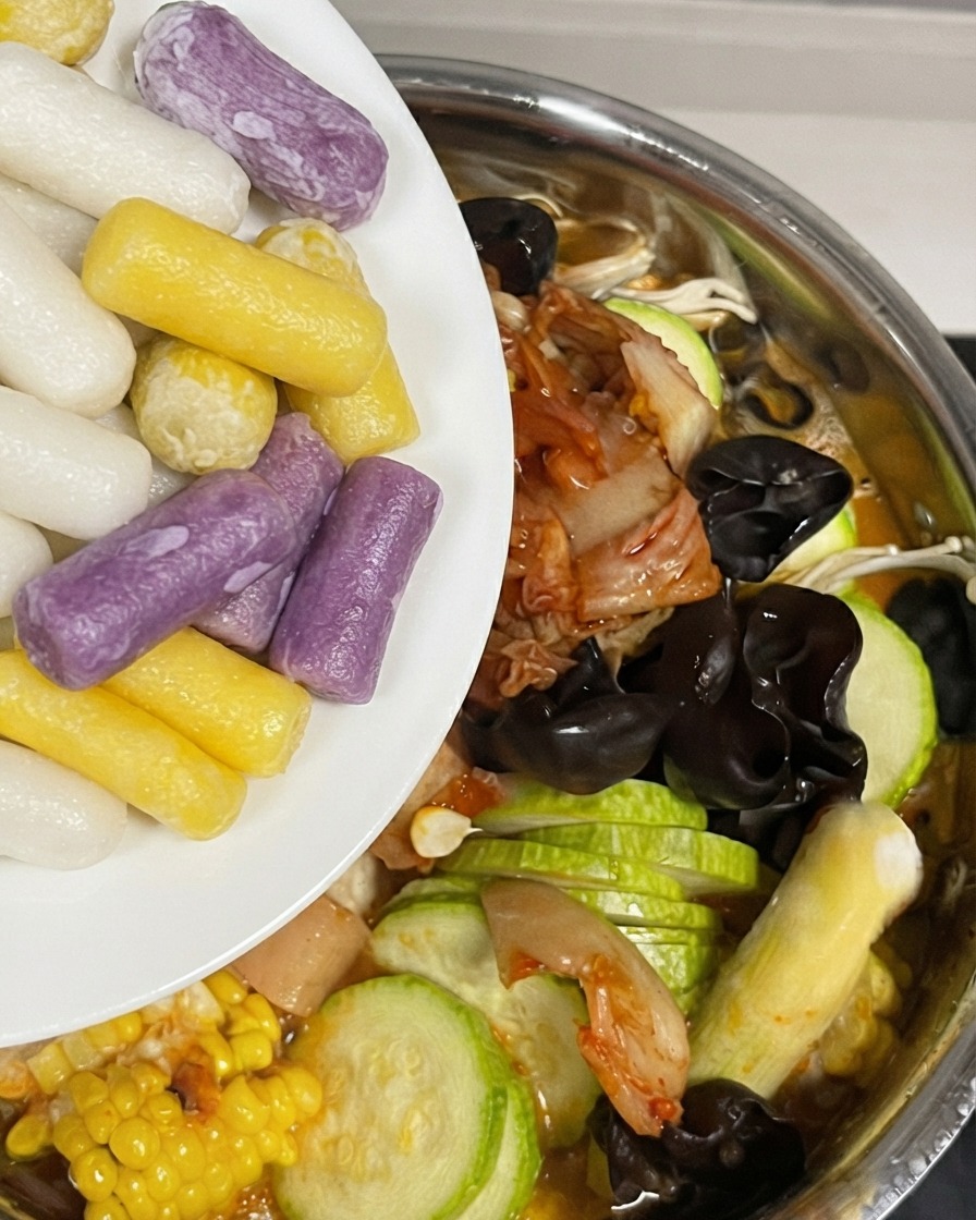 Adding colorful cheese rice cakes into the pot filled with ingredients and sauce.