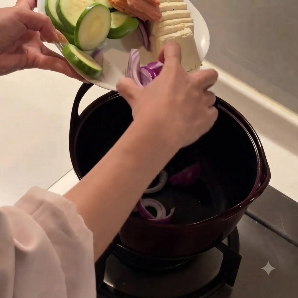 Sliced red onions being placed into the bottom of a dark cooking pot.