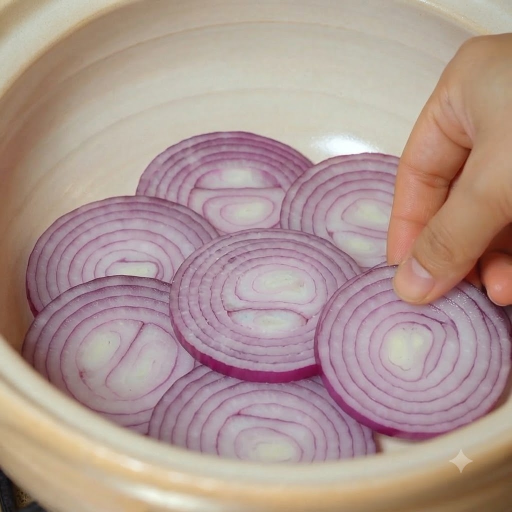 Sliced red onion pieces being arranged at the bottom of an earthenware pot.