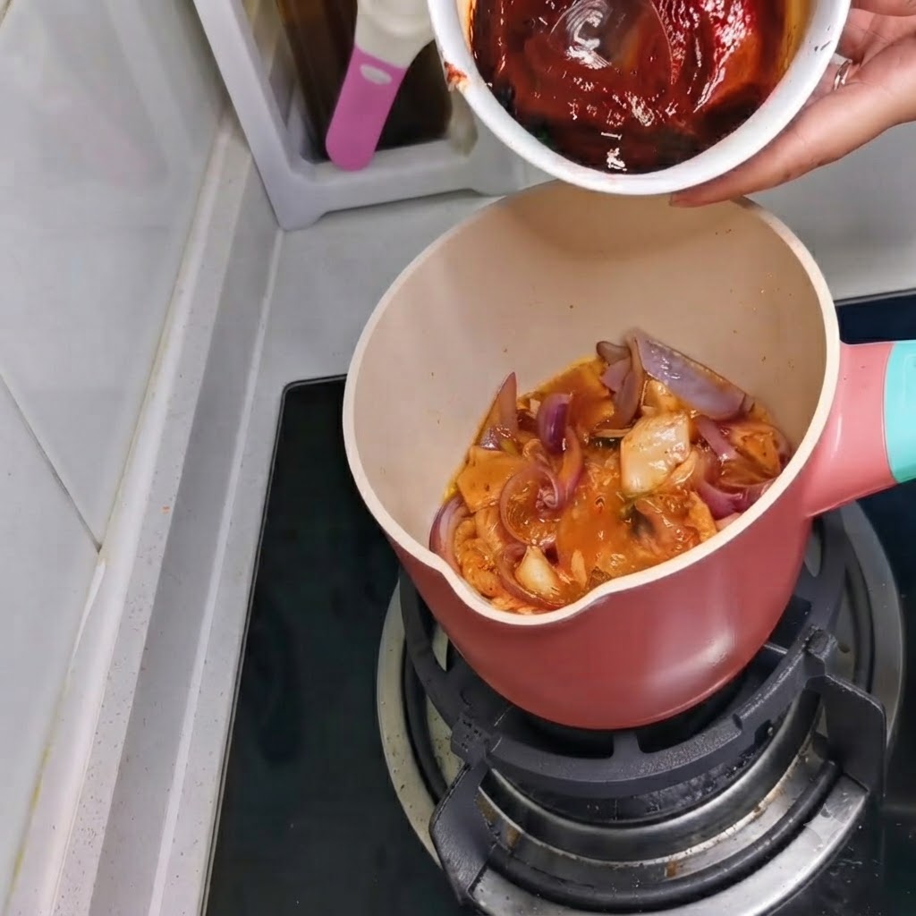 A bowl containing a dark red sauce mixture being poured into the pot.