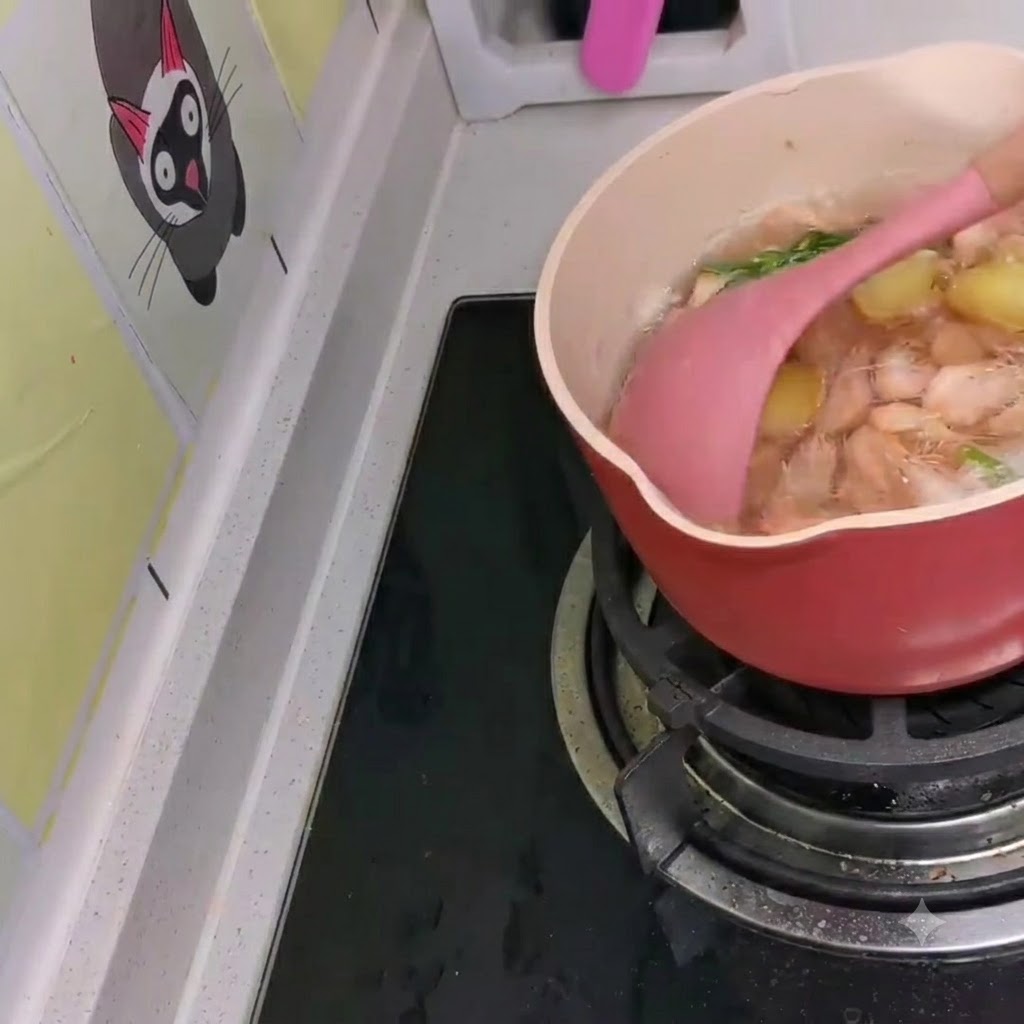 Small white shrimp being stirred into a simmering pot of Korean-style ramen using a pink spatula.