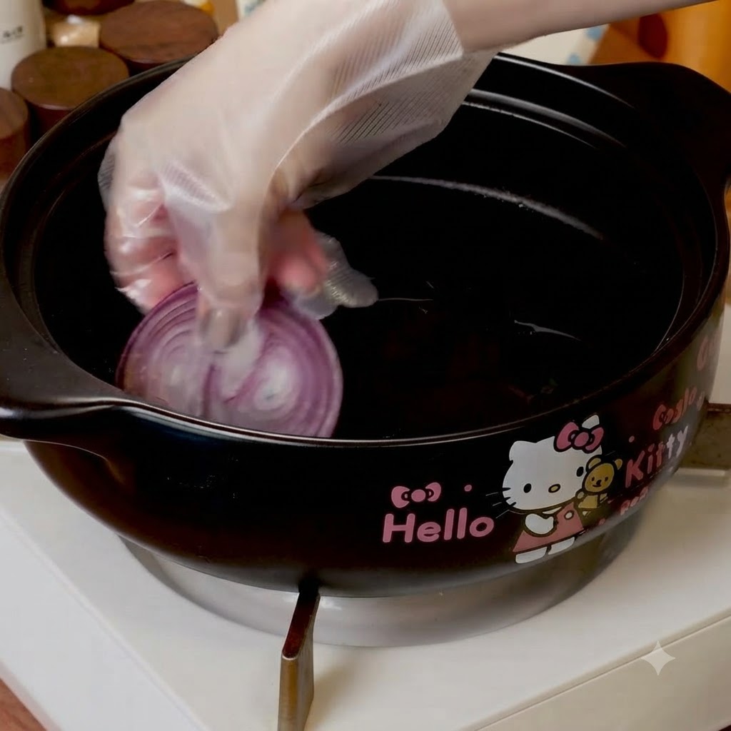 Slices of red onion being placed at the bottom of a black cooking pot.