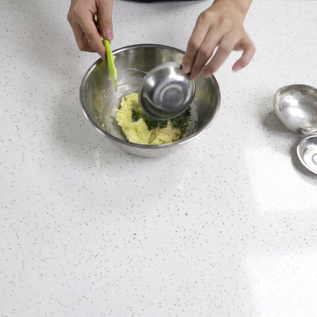Pouring and mixing seasonings into the butter using a spatula and small metal bowl.