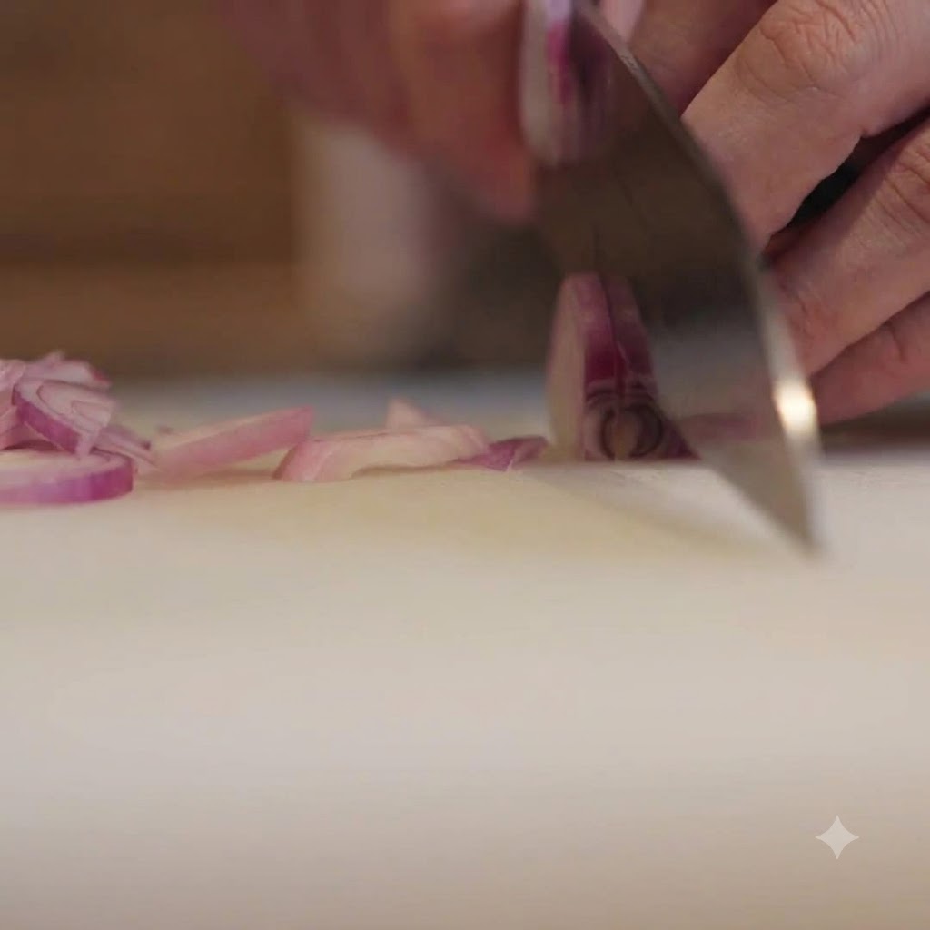 A chef slicing red onions on a cutting board with a knife.