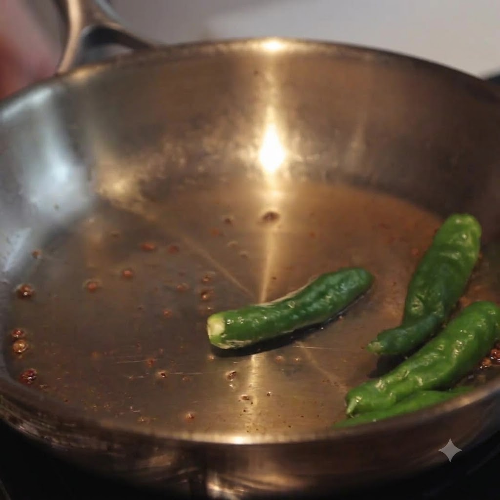 Shishito-style green chili peppers frying in a stainless steel skillet with residual pan juices.