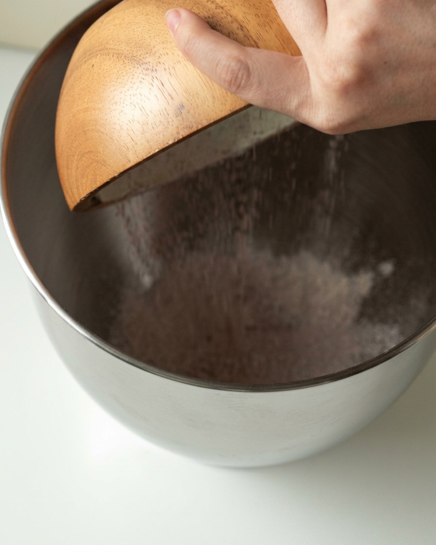 Bread flour, organic raw sugar, yeast, and plant-based milk being poured into a large mixing bowl.