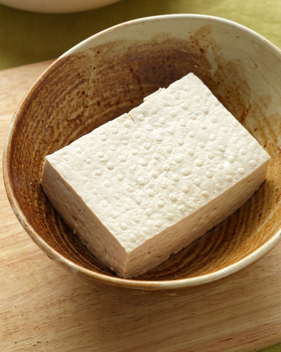 A block of firm tofu resting inside a textured ceramic bowl.