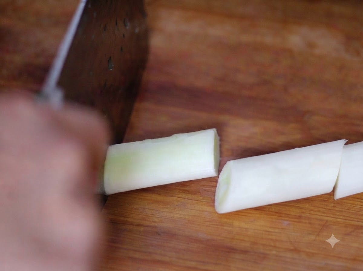 A cleaver slicing through fresh green onion sections on a wooden board.
