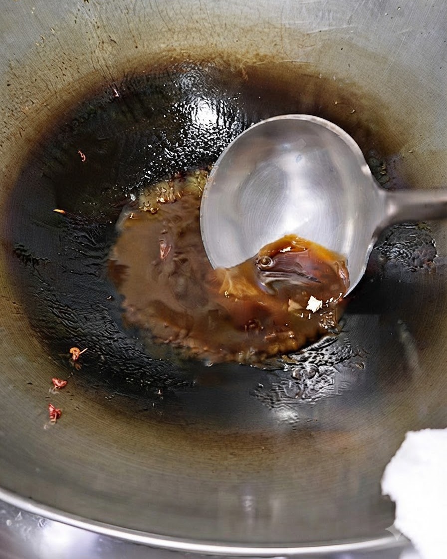 A ladle pouring water starch slurry into a seasoned sauce bubbling in a wok.
