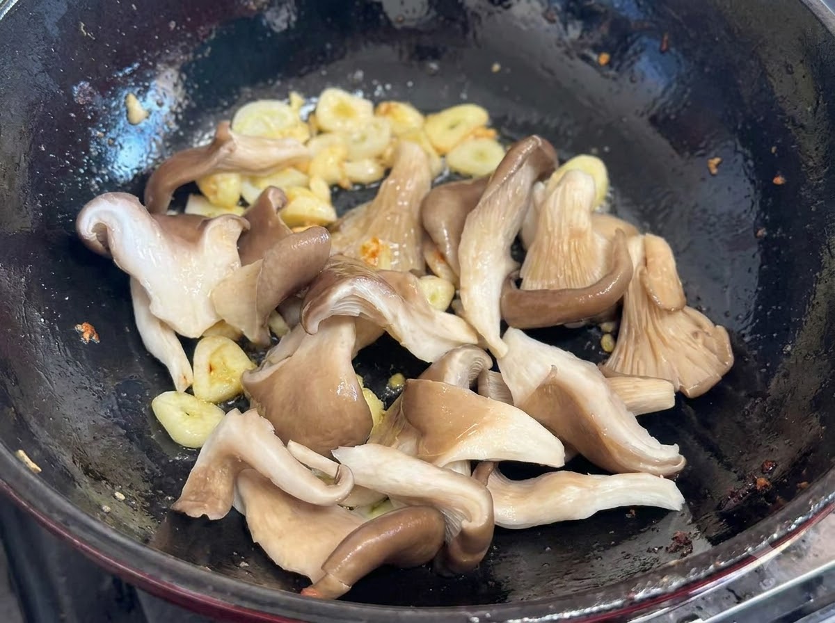 Fresh oyster mushrooms added to the wok with garlic and scallions.