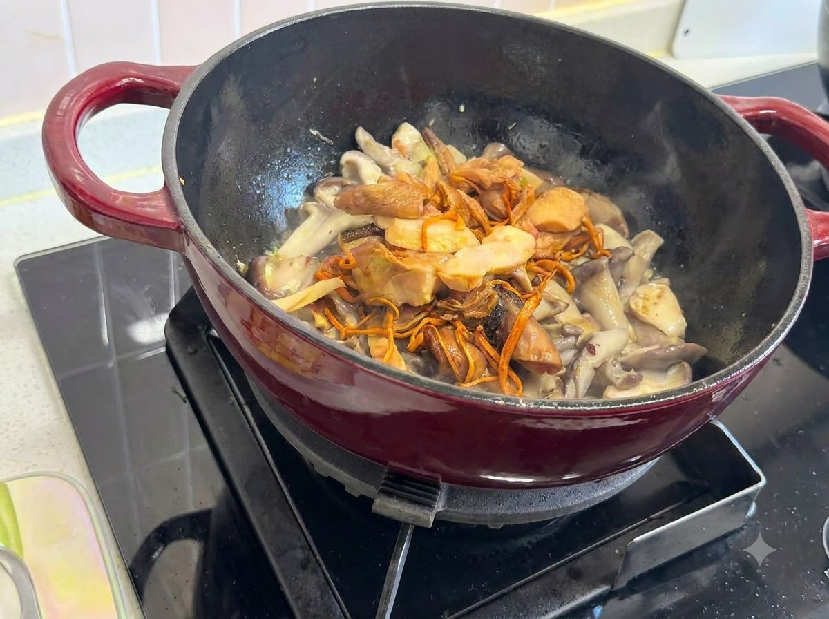 Rehydrated mixed dried mushrooms placed on top of the fresh mushrooms in a red-handled pot.
