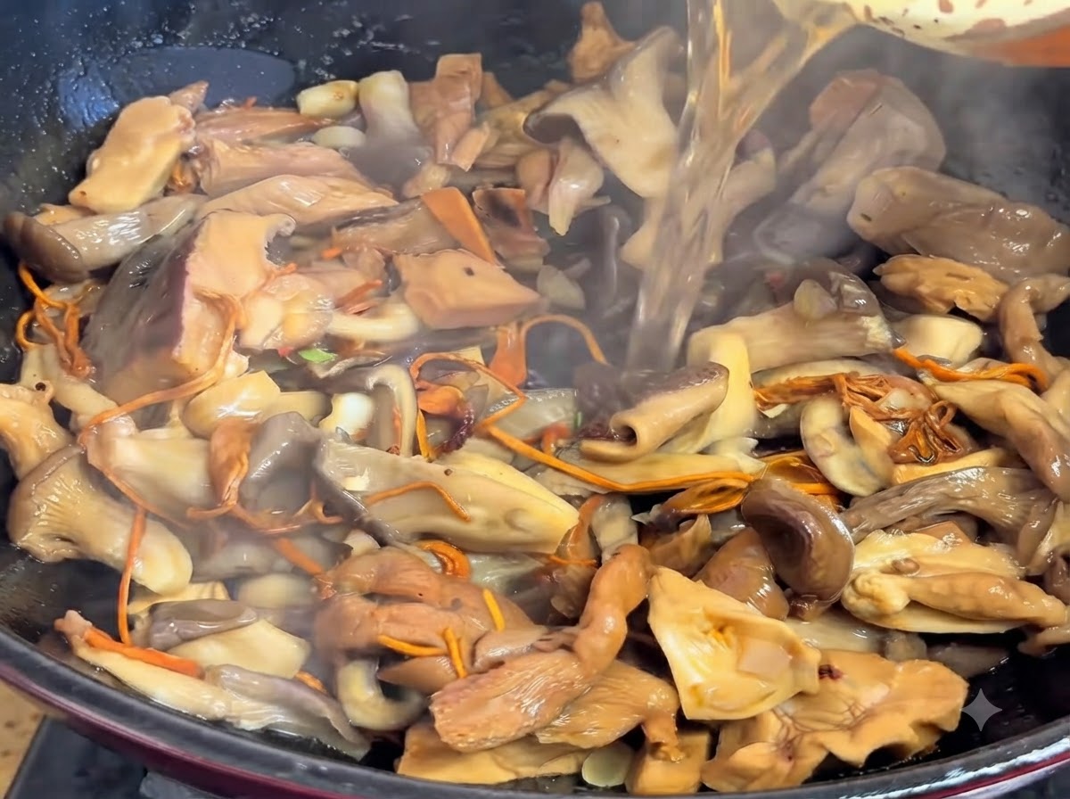 Clear liquid being poured into the pot filled with cooked mushrooms.