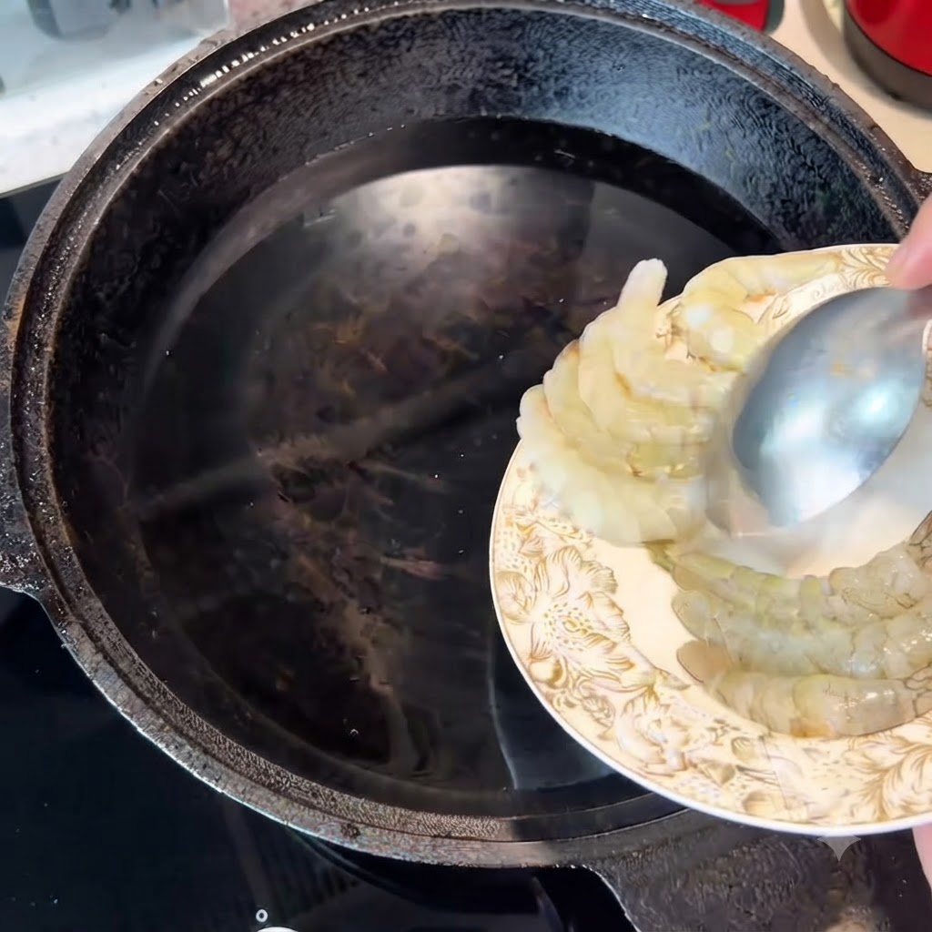 Raw shrimp being transferred with a spoon into a pot of cold water.
