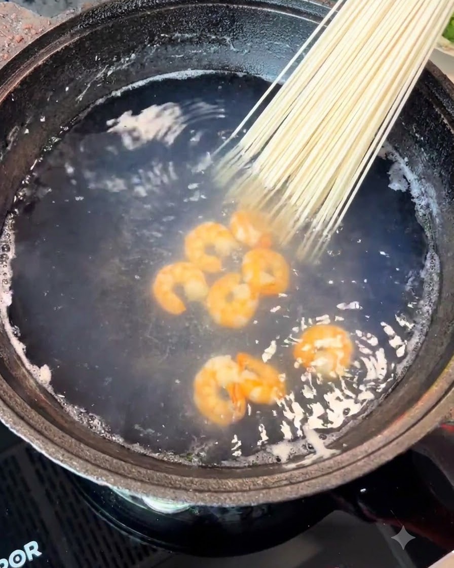 A bundle of dried noodles being placed into the pot along with the shrimp.