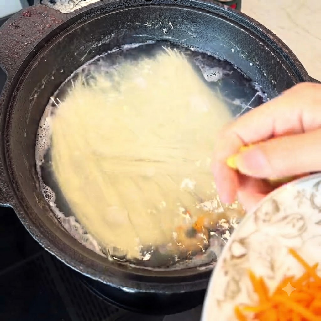 Julienned ginger being added into the boiling noodle pot.
