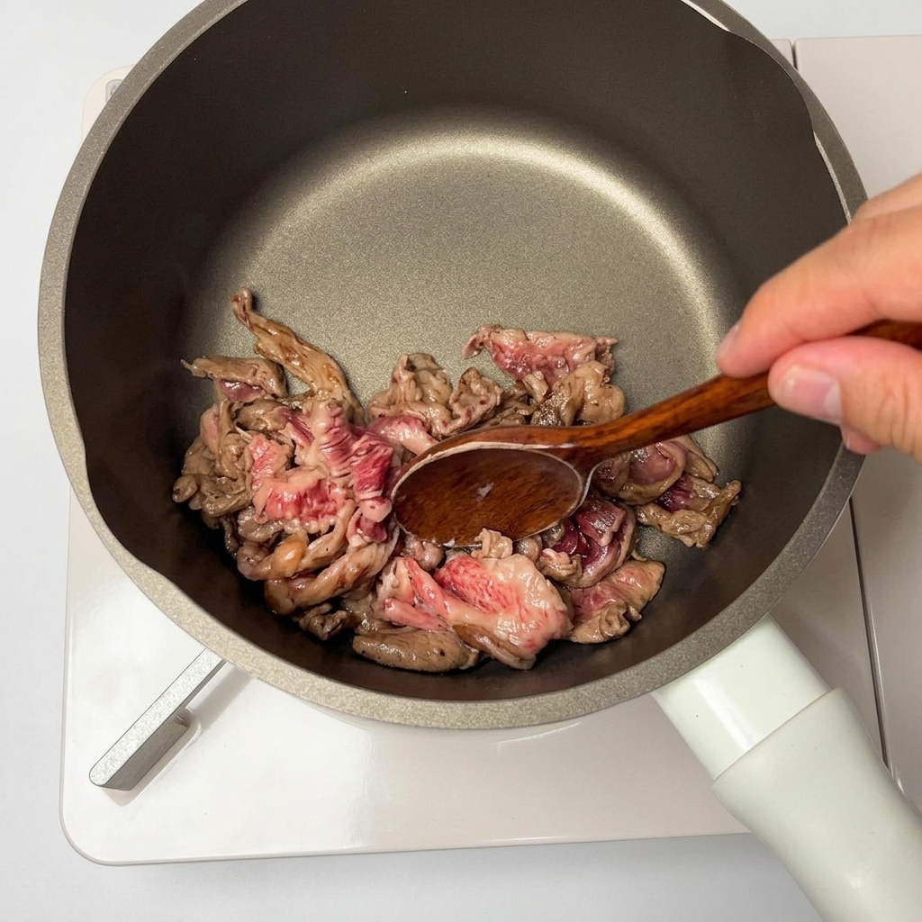 Marinated beef slices being stir-fried in a non-stick pan with a wooden spoon.