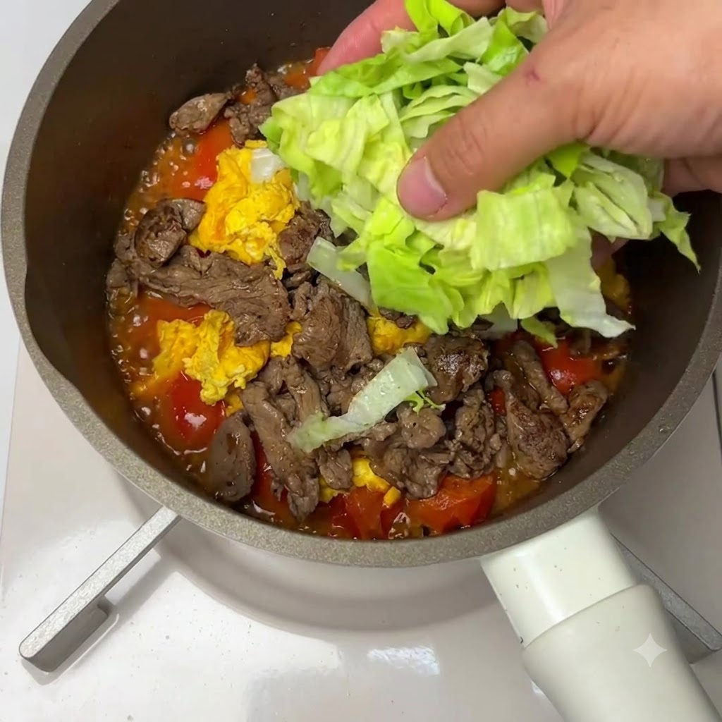 Chopped lettuce being placed over a mixture of beef, eggs, and tomatoes in a pan.