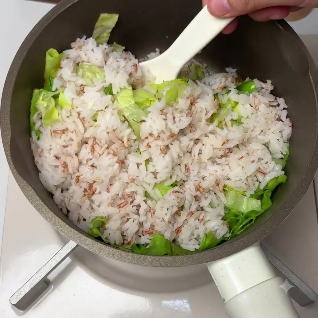 Cooked rice, fresh lettuce, and the tomato mixture being thoroughly combined in a pan with a white spatula.