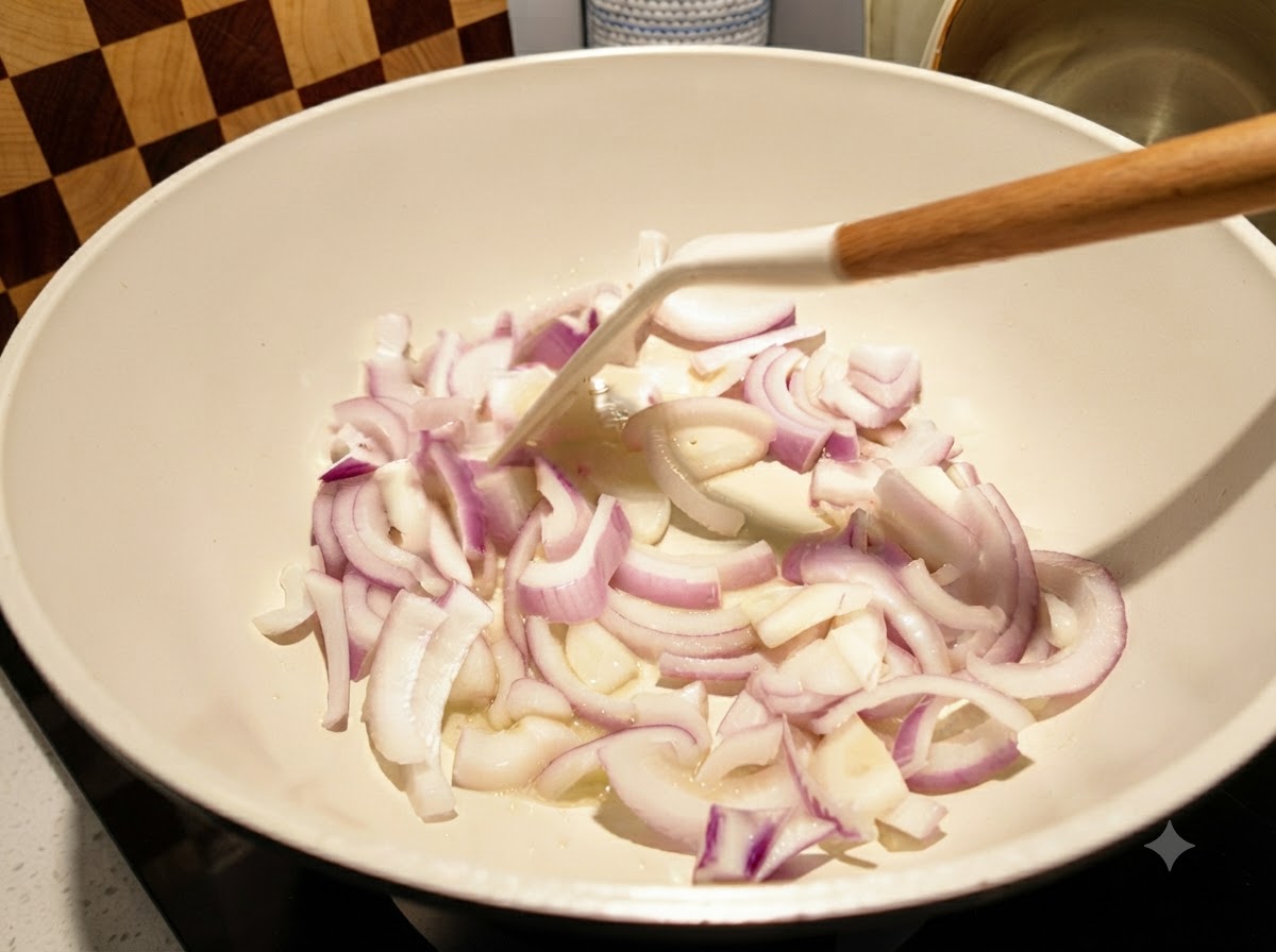 Sliced red onions being stir-fried in a white pan with a white spatula.