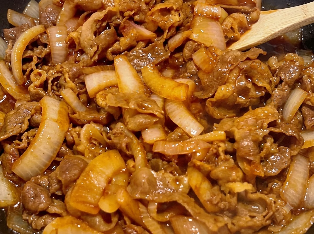 Beef and onions being stirred with a wooden spatula while simmering in a thick dark brown sauce.