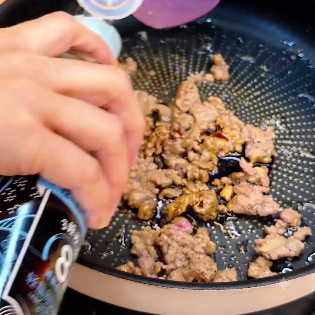 A bottle dispensing soy sauce over the browned ground beef in the pan.