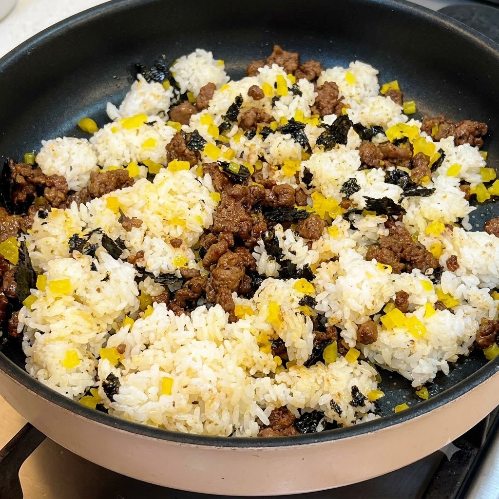 Salad dressing being drizzled in a zigzag pattern over a pan containing rice, beef, and yellow radish.