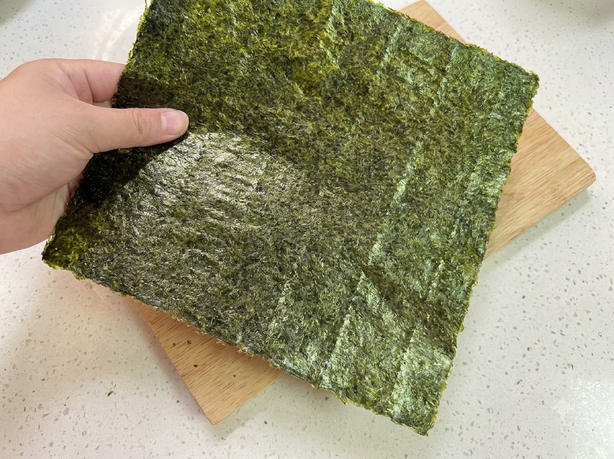 A sheet of dry seaweed held over a wooden cutting board.