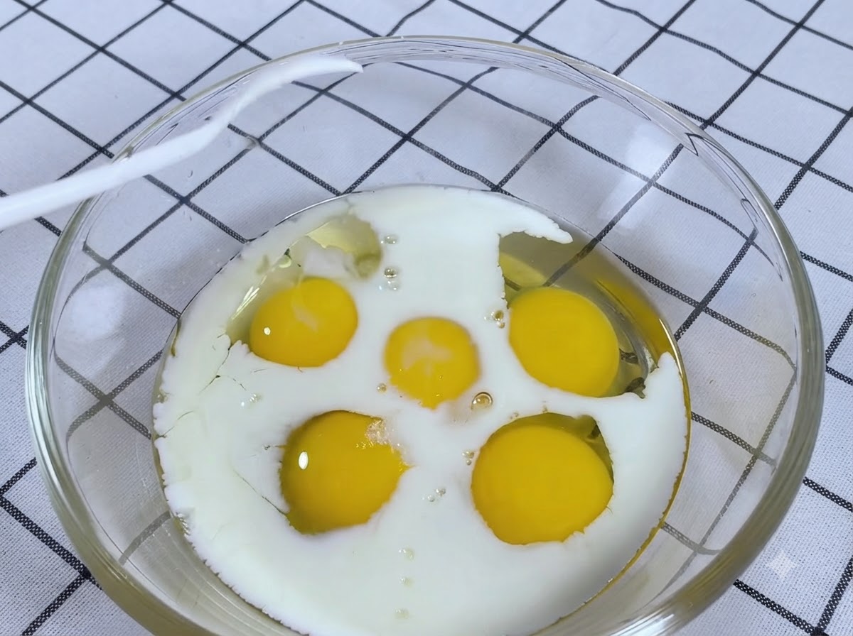 A spoonful of salt being added into a glass bowl with cracked eggs and milk.