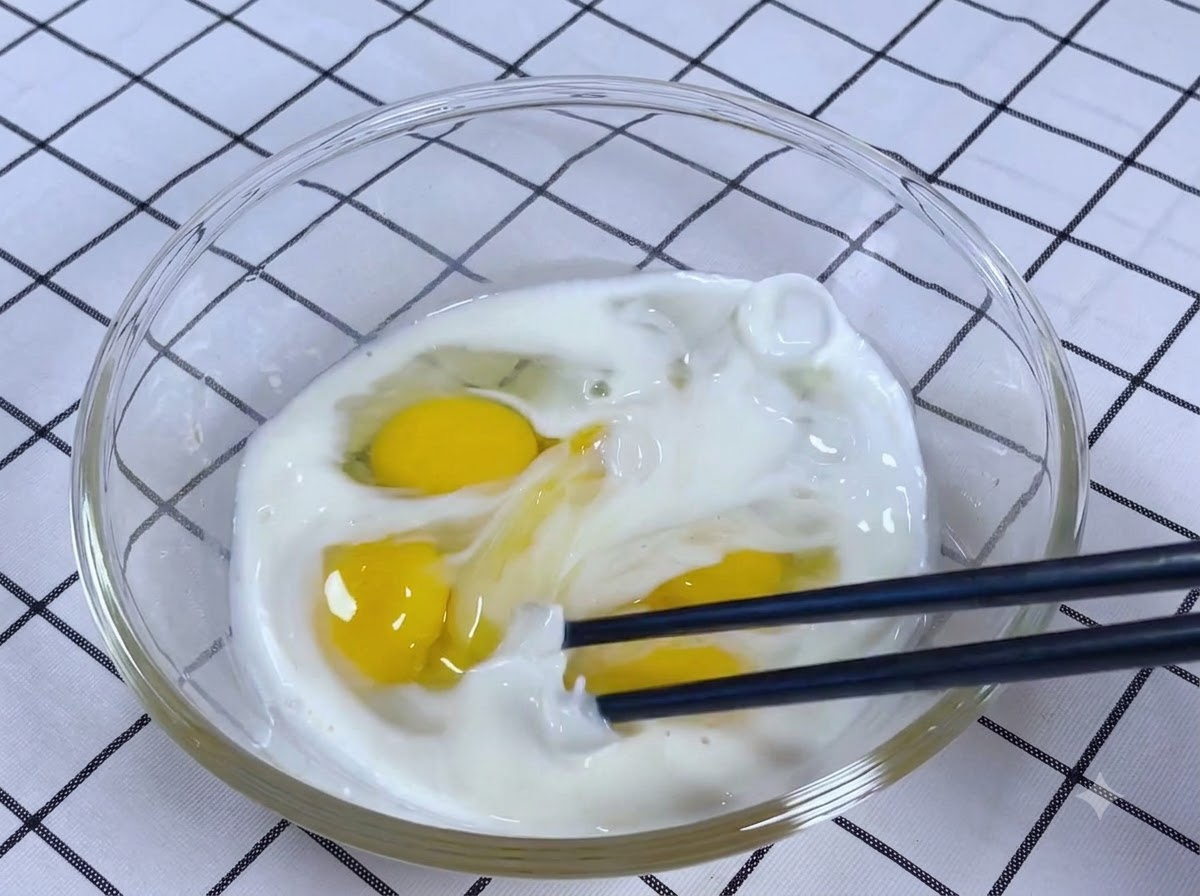 Chopsticks thoroughly whisking a mixture of eggs, milk, salt, and sugar in a glass bowl.