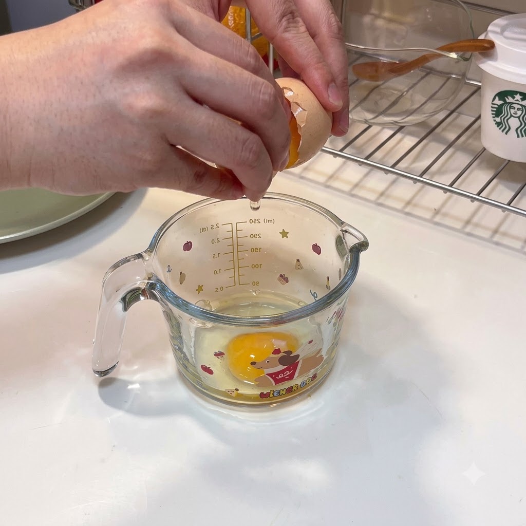 Two eggs being cracked into a measuring cup with cornstarch water being poured in.