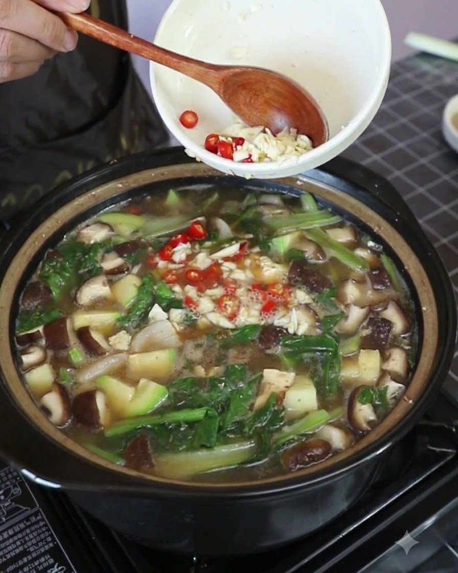 Minced garlic and bright red Thai chili pieces being tipped into the simmering stew.