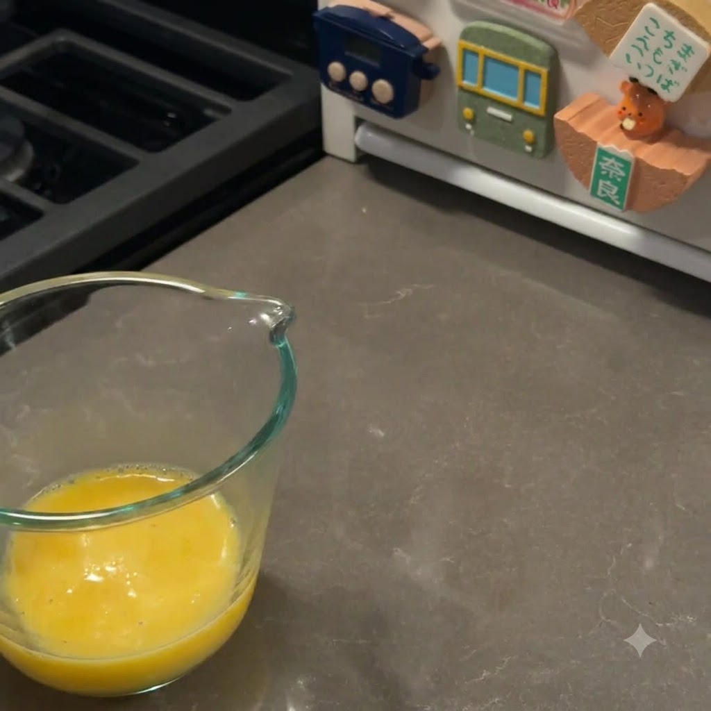 A glass measuring cup filled with freshly whisked yellow egg wash sitting on a kitchen counter.