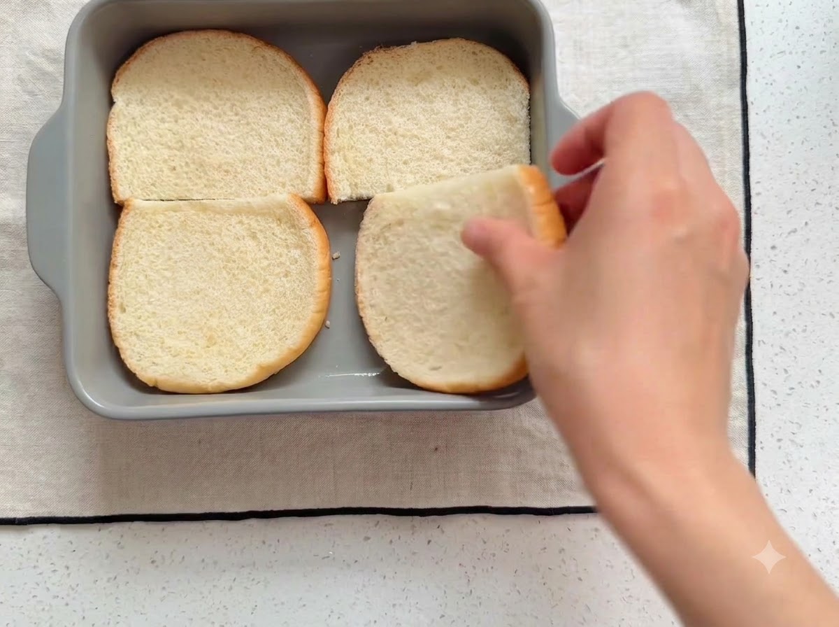 Burger buns cut in half and placed neatly inside a grey square baking dish.