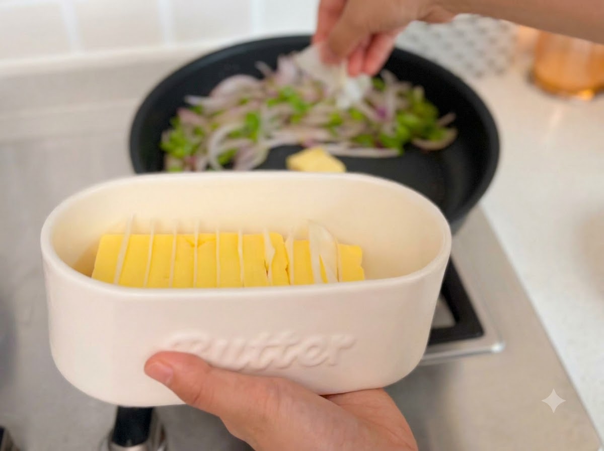 Slices of raw beef being added to a frying pan containing butter and sautéed vegetables.