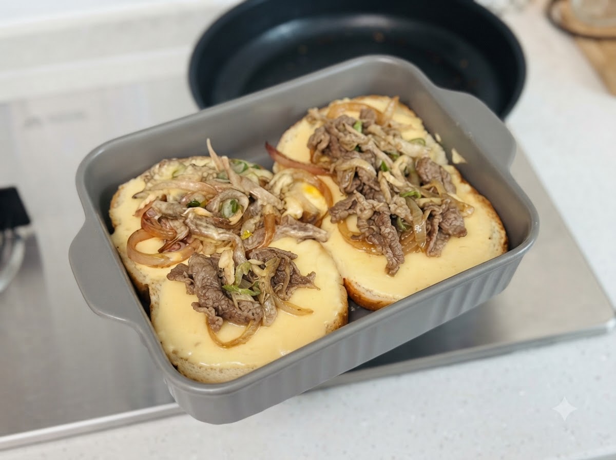 Cooked meat and cheese mixture being spooned onto burger buns inside a grey baking dish.
