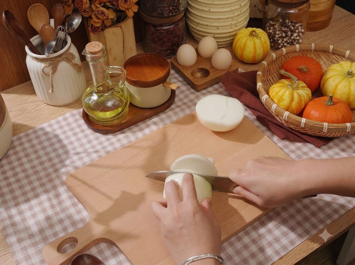 A close-up view of hands slicing a white onion on a wooden cutting board with a sharp knife.