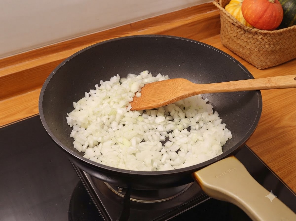Chopped onions being stirred with a wooden spatula inside a black frying pan on a stove.