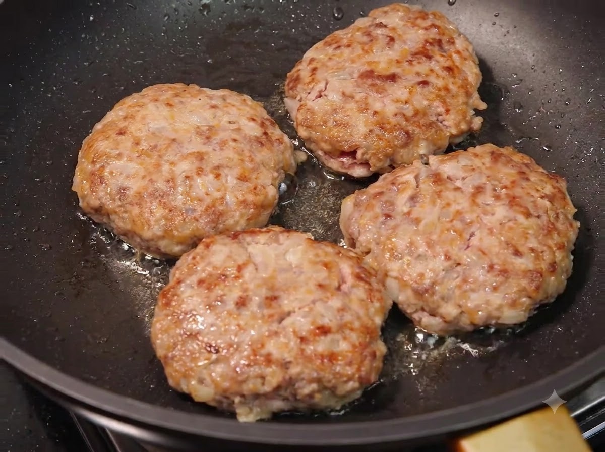 Four meat patties frying in a pan, displaying beautifully browned and caramelized crusts.