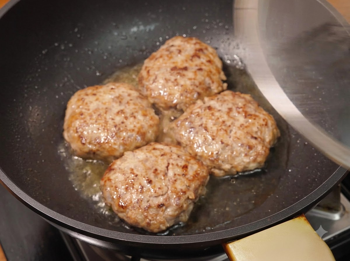 A glass lid being placed over four browned meat patties in a hot pan.