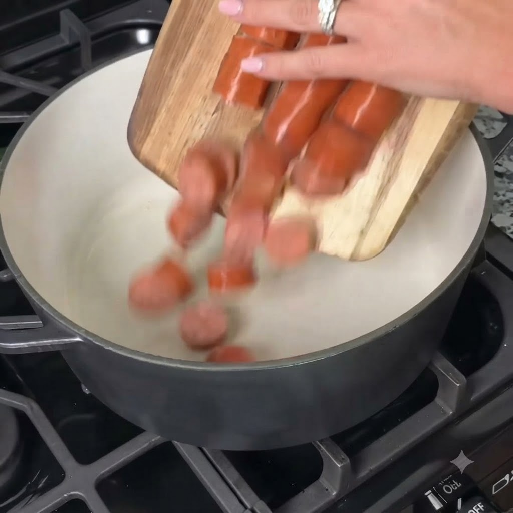 Sliced sausage being poured from a cutting board into a large cooking pot on the stove.