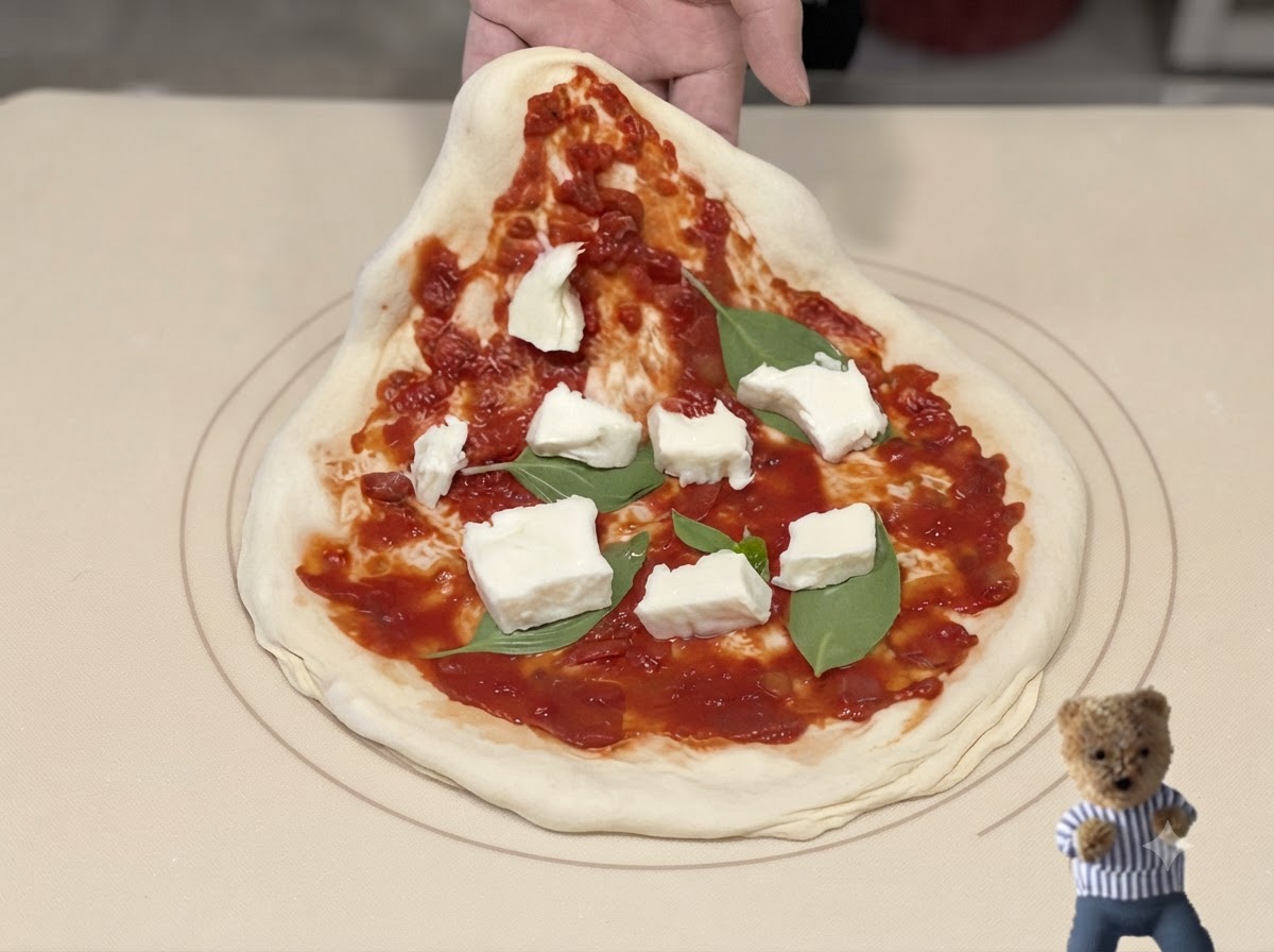 A metal pizza peel sliding underneath an assembled pizza with sauce, basil, and cheese.